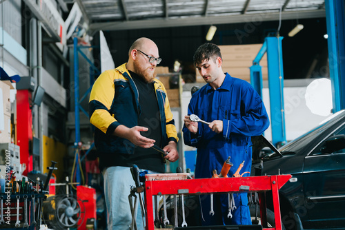 Professional mechanic specialist and apprentice during car repair session working with focus at garage shop to fix vehicle engine problem