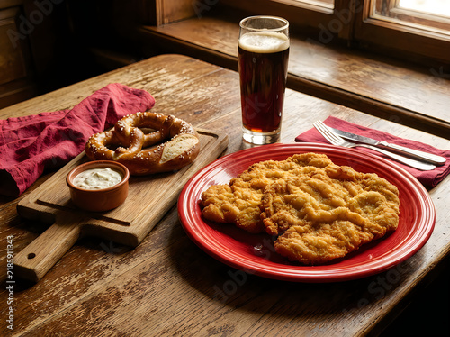 Schnitzel with pretzel and dark beer on a wooden table