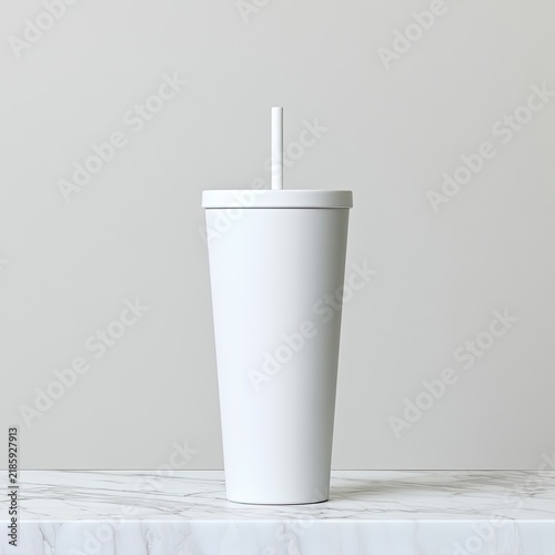 A simple, matte white reusable tumbler with a straw stands on a marble surface