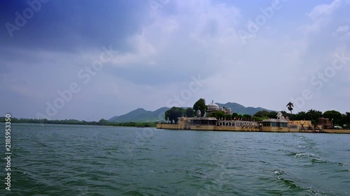 Udaipur, Rajasthan, India: Jag Mandir recedes across Lake Pichola, with a trail of disturbed water in the foreground and green hills behind the island.