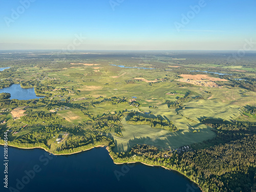 Aerial view of a wide river, green forest and fields under clear blue sky. Scenic countryside, nature landscape, summer air travel, peaceful outdoors. Background with copy space
