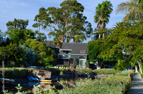 Scenic Waterfront House Surrounded By Lush Tropical Trees Along Calm Residential Canal In Sunny Coastal Neighborhood Setting