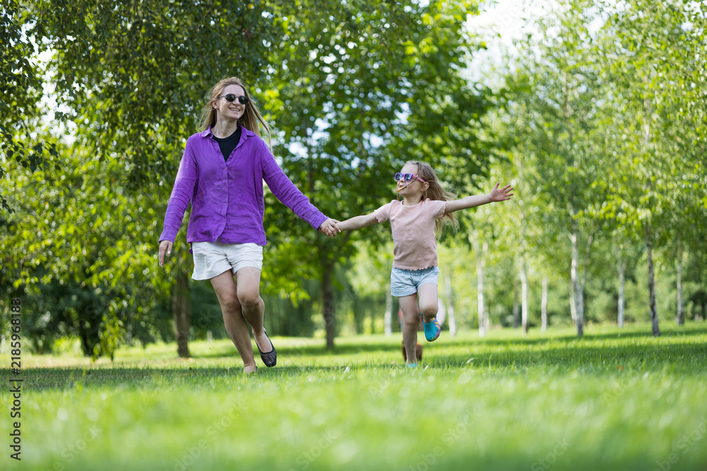 Fototapeta premium Full length view of mother and little daughter running together outdoors