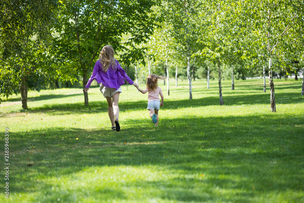 Fototapeta premium Distant shot of mother and young daughter running hand in hand in park