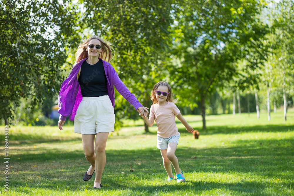 Fototapeta premium Full length view of mother and daughter walking towards camera in sunny park