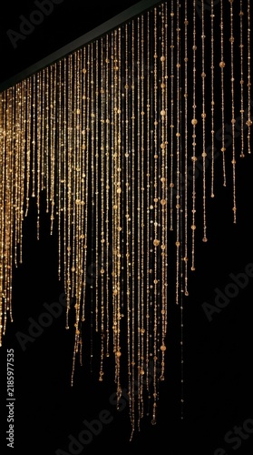 Gold beaded curtain hanging from dark ceiling against black background