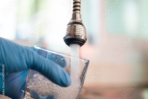 Water quality testing with a gloved hand collecting a clean water sample from a faucet.