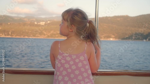 Girl on a boat looking at hills and water during sunset near a coast