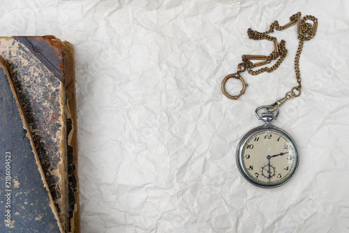 Fotografie Vintage pocket watch with chain and old antique book on crumpled paper background