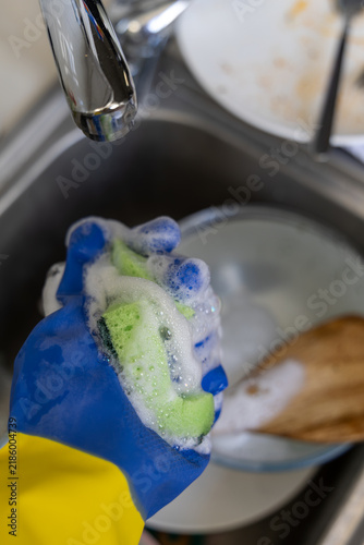 Fotografía gloved hand holding soapy sponge with rich foam for dishwashing in messy kitchen