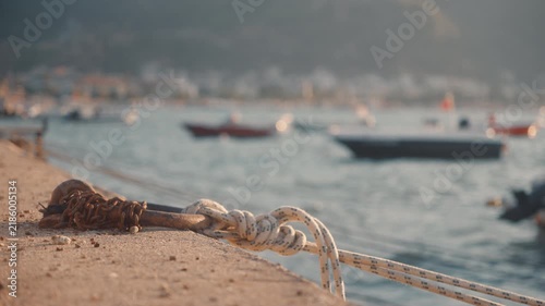 Rope tied to a post at a busy harbor with small boats floating in the water during late afternoon