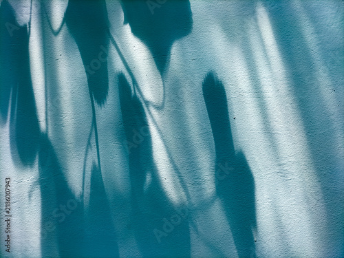 Abstract backdrop of blurry leaf shadows interacting with bright sunlight on a textured blue concrete wall.