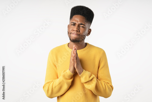 Cuadro en lienzo Young African man holding hands together in a pleading gesture isolated over whi