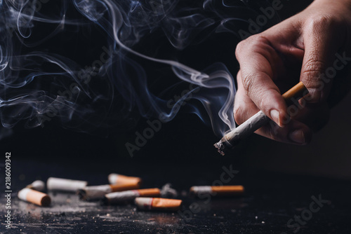 Fotografía Hand Holding Smoking Cigarette with Heavy Smoke on Dark Background
