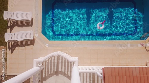 Top down shot of colorful inflatable unicorn float is in the pool while sun loungers sit nearby in a backyard during the day
