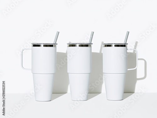 Three identical white insulated tumblers with handles and straws on white background