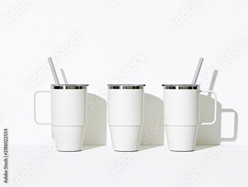 Three white insulated tumblers with lids and straws on a white surface