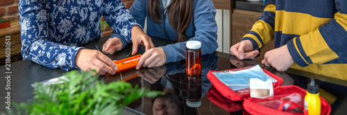 Unrecognizable mother showing how to use medical injection with pre filled syringe to her children while organizing domestic first aid emergency kit, providing healthcare guidance and education.