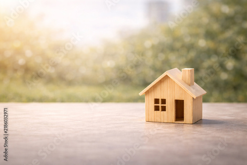 Small wooden house model on a table with soft natural sunlight and blurred green background. Concept of real estate, home ownership, property investment, mortgage and buying a new house with copy spac