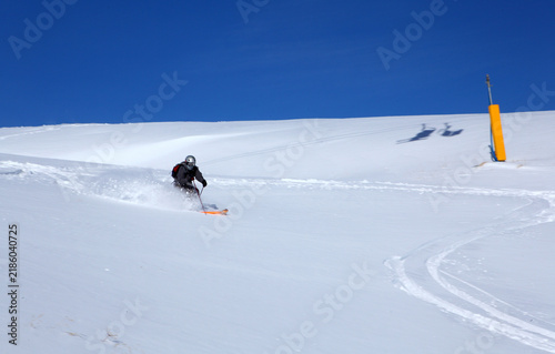 Obraz na płótnie Skier carving down a snow covered mountain slope on a sunny winter day under blu