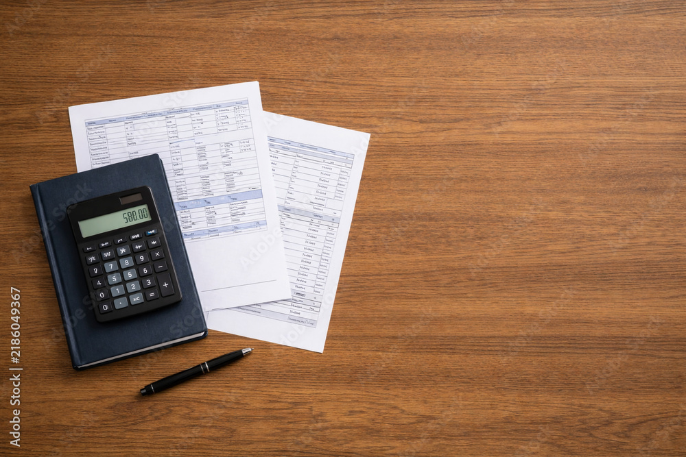 Obraz premium Top view of calculator, financial documents, notebook and pen on a wooden office desk with large copy space. Accounting, budgeting, tax calculation, financial planning and business paperwork concept.