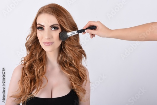 Foto Attractive, shapely model with long red hair being made-up in the studio