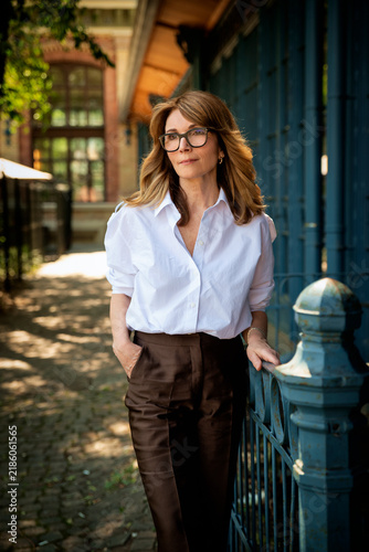 Elegant mature businesswoman in white blouse and brown pants standing between blue doors
