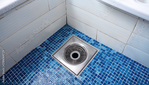 close up mosaic blue tiled floor with square metal drain cover circular indentation center contrasting clean white wall tiles modern bathroom design and functionality