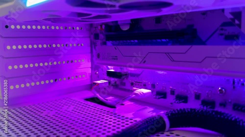 A close-up of the interior of a gaming PC bathed in vibrant RGB colors: motherboard, graphics card, cooling fans, cables, and perforated case panels. Computer hardware, RGB lighting, technology.