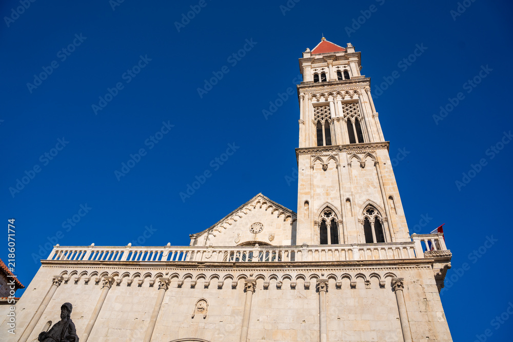 Obraz premium Tower of St. Lawrence Cathedral in Trogir, Croatia, featuring intricate stonework and a red-tiled roof against a clear blue sky