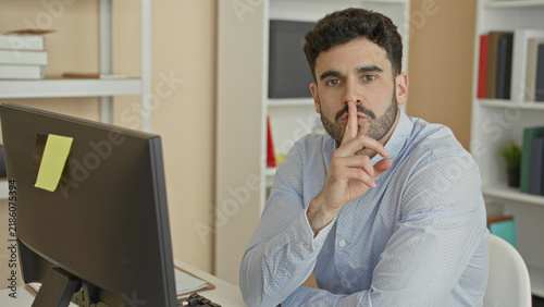 Cuadro en lienzo Man at computer with finger to lips performing shushing gesture in office building; quiet concentration