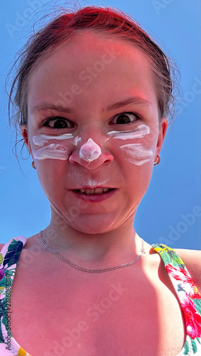 Cute happy teenager girl applying sunscreen cream on face beach lifestyle portrait.