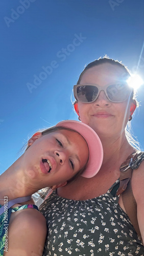Happy mother and daughter taking silly selfie on sunny summer vacation.