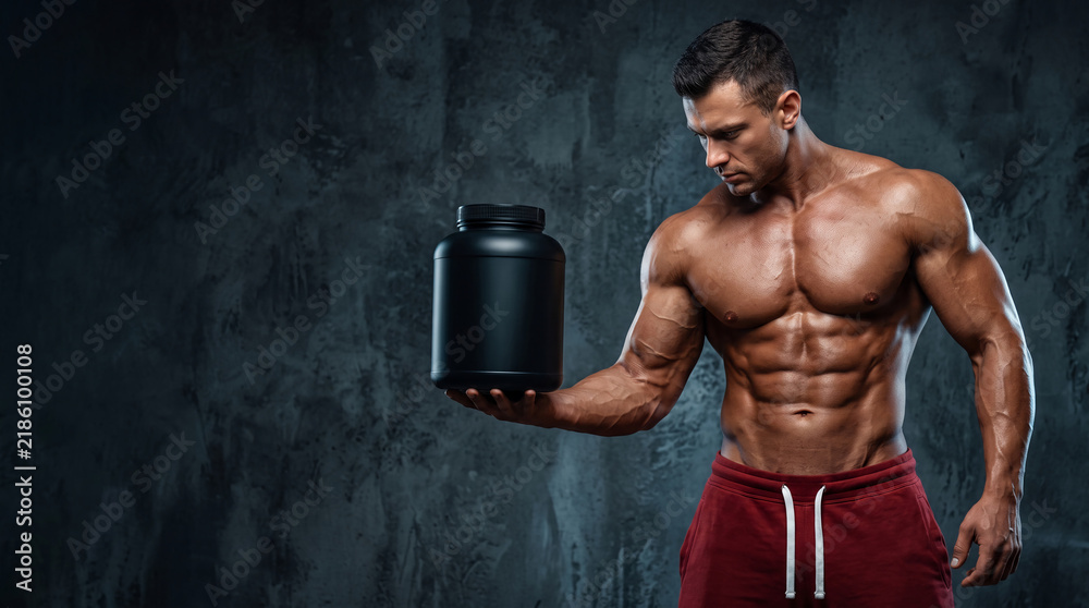 Obraz premium Muscular shirtless male bodybuilder holding blank black protein powder tub mockup for sports nutrition advertising against dark grunge background fitness supplement and extreme gym strength concept