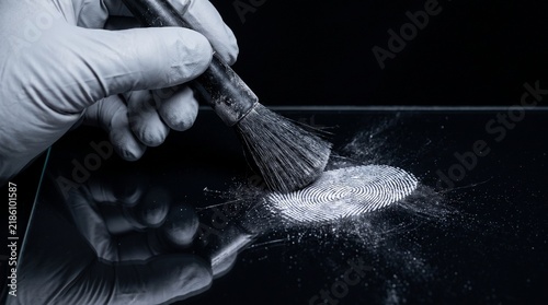 Gloved hand dusting fingerprint with brush on black surface with law enforcement crime scene holds brush identification investigation collection forensic evidence analysis