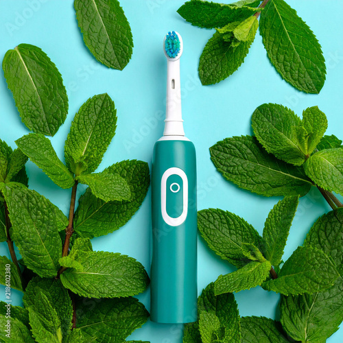 the image showcases an electric toothbrush lying on a blue surface. the toothbrush has a white head and a teal handle featuring a white button