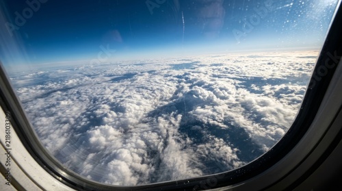 Aerial View of Fluffy White Cumulus Clouds from Airplane Window over Clear Blue Sky Background
