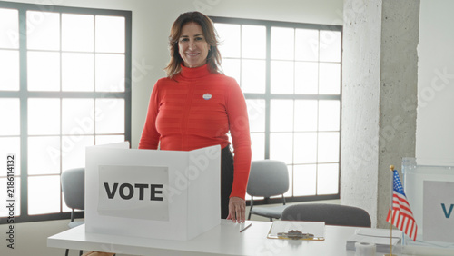 Fotografía Woman gives thumbs up at a voting booth with visible vote sign and sticker, hand resting on ballot screen in a public building; civic pride