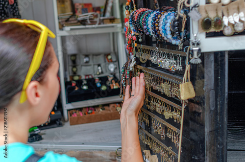 A woman touches handmade earrings displayed on a stand inside a jewelry shop.