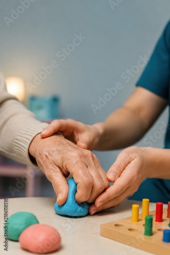 Occupational therapist guiding senior's hand with therapy putty