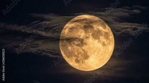 Full harvest moon peeking through dark clouds in a starry night sky. Golden moon shrouded in nighttime mist. Lunar background