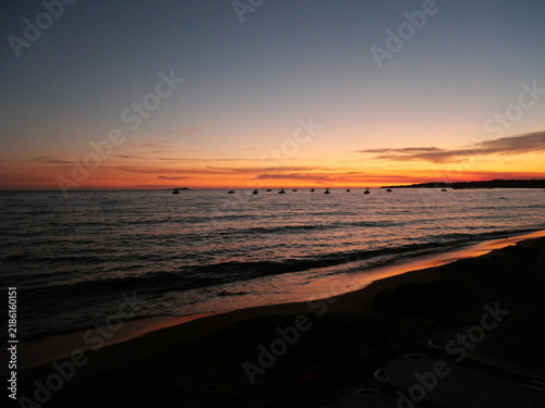 Foto Coucher de soleil paisible sur l'océan avec des teintes orange et roses se reflétant sur l'eau et de petits bateaux en silhouette à l'horizon