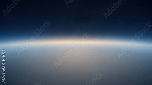 A wide angle view of the thin blue atmosphere of earth seen from space with a glowing horizon line and dark black sky