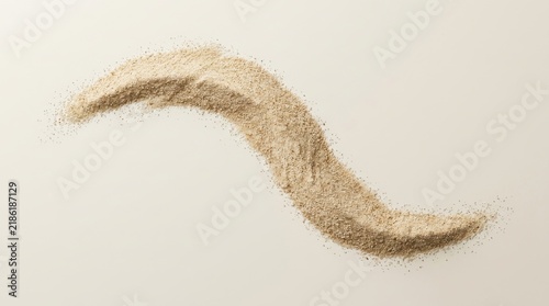 A wavy line of beige sand or ground grain isolated on a light background showing texture and natural organic particles