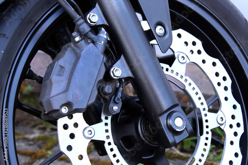 Close-up of motorcycle front wheel featuring silver perforated brake rotor, dark caliper, black fork, alloy hub, ABS ring, and rugged tire with metallic details. Close-up motorcycle wheel. Motorcycle 
