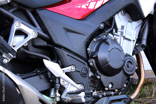 Black motorcycle engine, Japanese motorcycle engine details: silver casing, red fairing, textured panel, copper pipe, metal bolt, footpeg, frame, gear shift lever, crank, cylinder, tube, sporty design