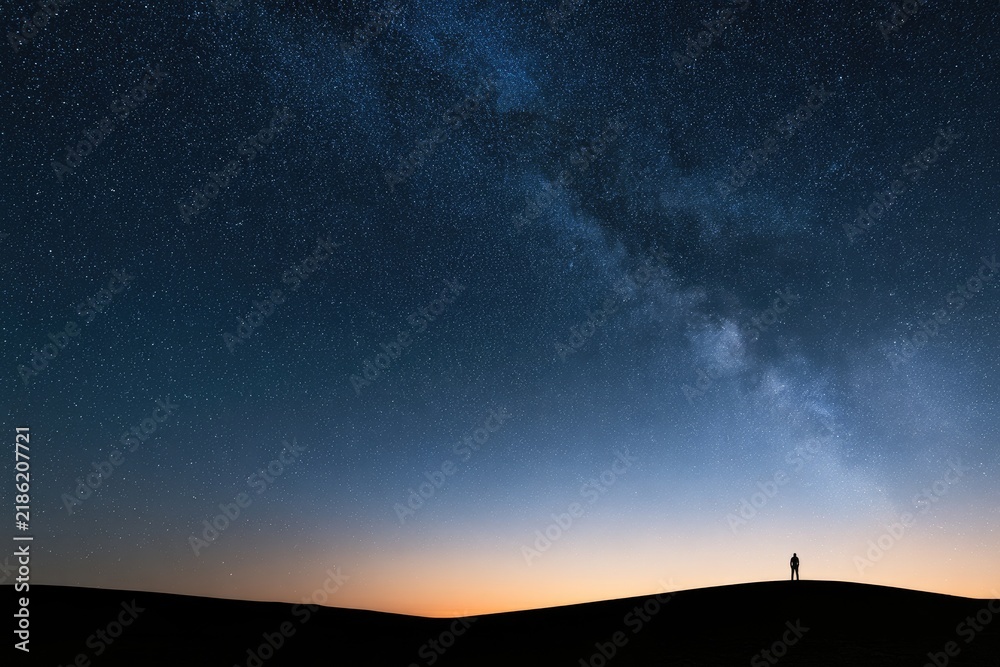 Obraz premium Lone figure silhouetted against a vast, star-filled night sky