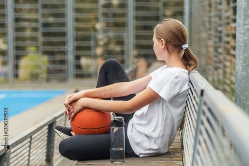 Basketball player resting alone outdoors with ball and water bottle