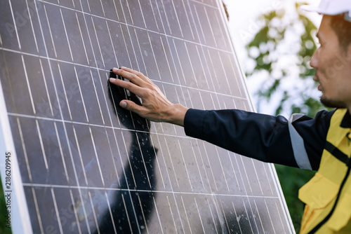 Technician in a yellow safety vest inspecting a solar panel outdoors, checking clean energy equipment during maintenance work.