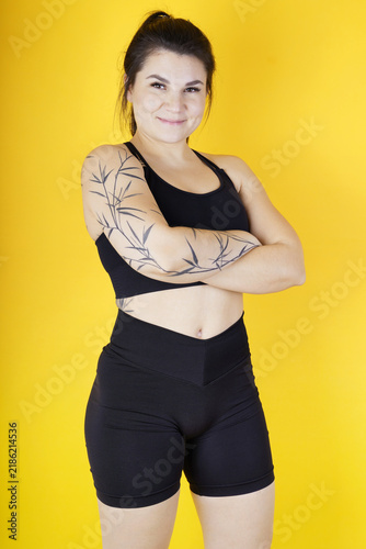 A athletic young woman with tattoos shows off her muscular body  the result of weight training at the gym  against a yellow background